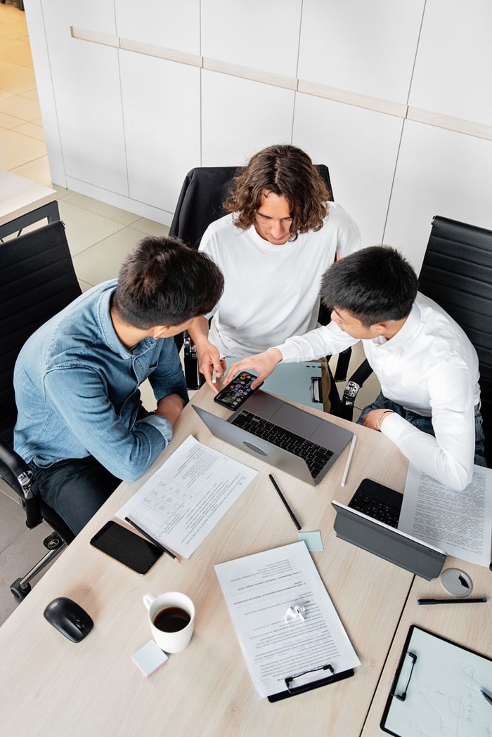 Overhead view of three colleagues collaborating at a desk with laptops and documents.